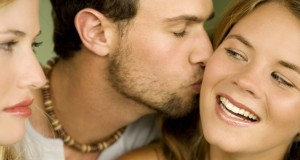 Young woman looking at man kissing smiling woman